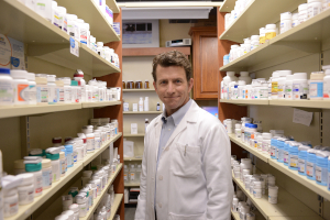 Pharmacist standing between pharmacy shelves filled with medication bottles