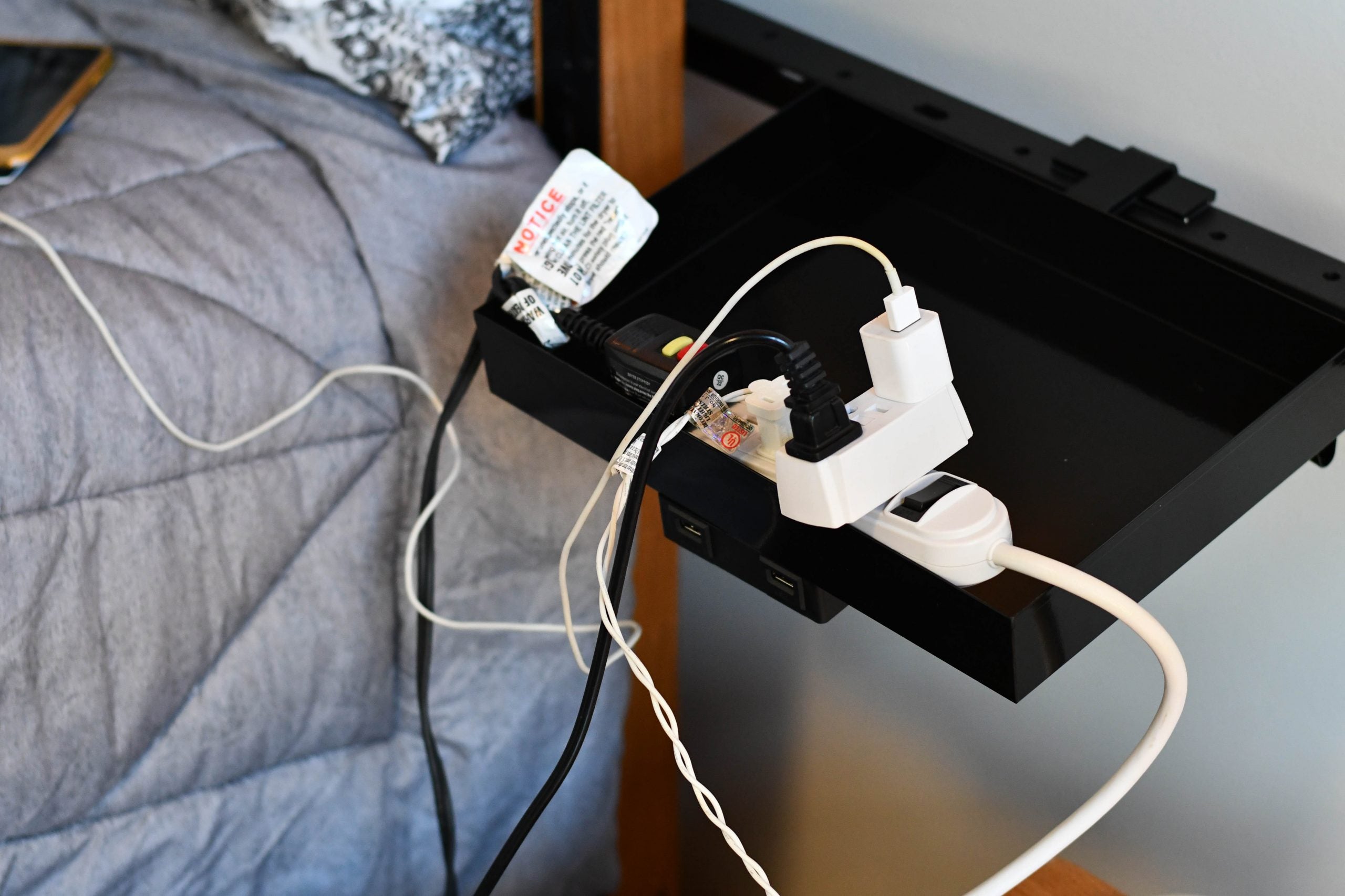 Power strip with too many cords plugged into it beside a bed