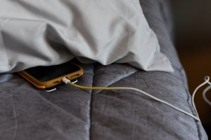 Smart phone charging under a pillow on a bed