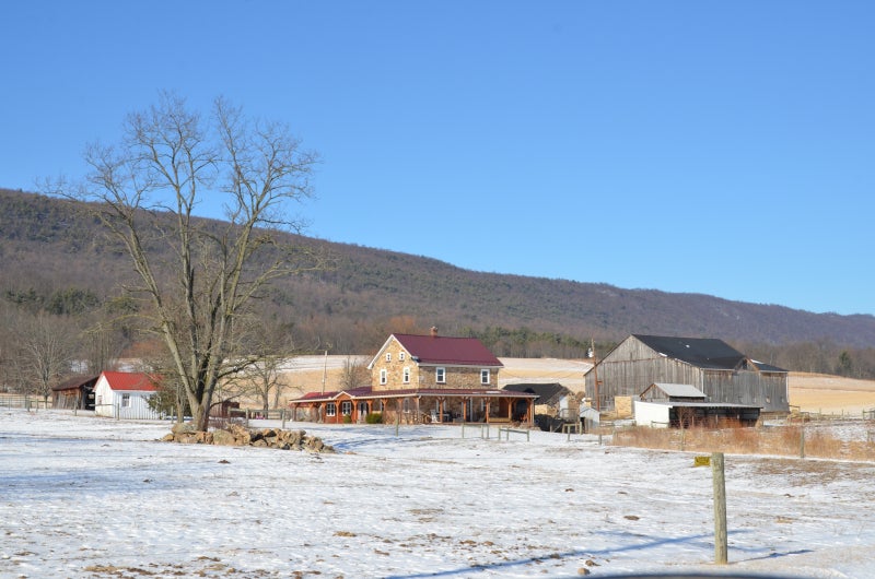 A farmhouse, barn, and sheds surrounded by lightly snow-covered fields