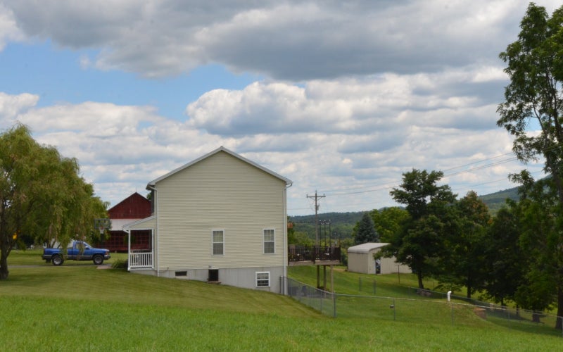A modern house and a red barn surrounded by green grass and trees with summer clouds gathering in a blue sky
