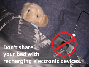 Don't share a bed with a charging electronic device. Not symbol over a cell phone in bed with a teddy bear.