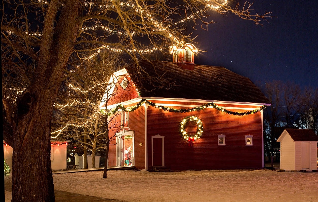 Red barn and tree branches adorned with white holiday lights.