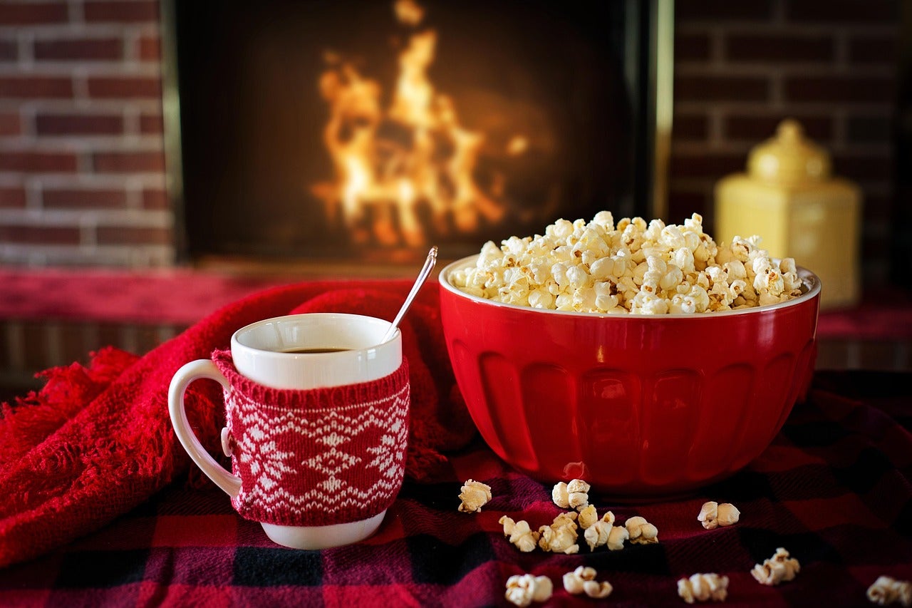 A bowl of popcorn and a holiday mug on a blanket in front of a fireplace.