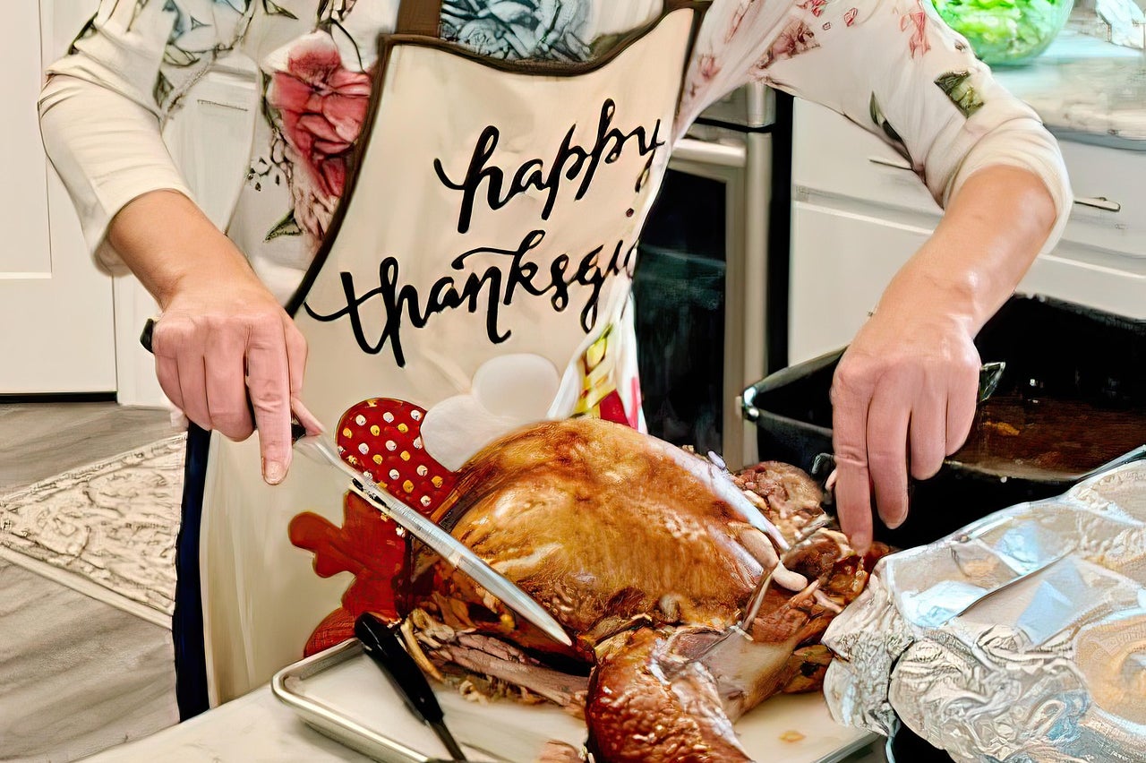A woman wearing a Happy Thanksgiving apron carves a roasted turkey.