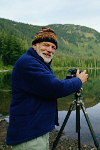 An elderly man taking a photo at a lake
